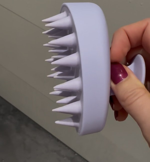 Lila Kopfhautbürste mit spitzen Noppen in der Hand