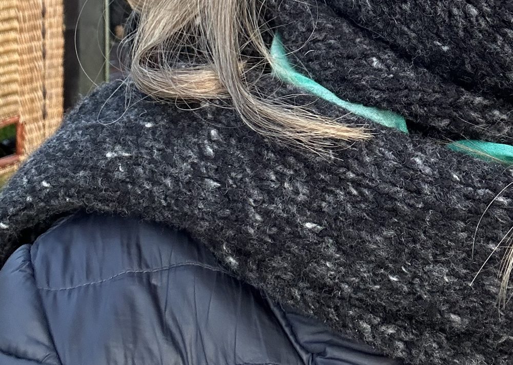 Trockene Haare im Winter: Haarsträhnen hängen im groben Strickschal über der Winterjacke